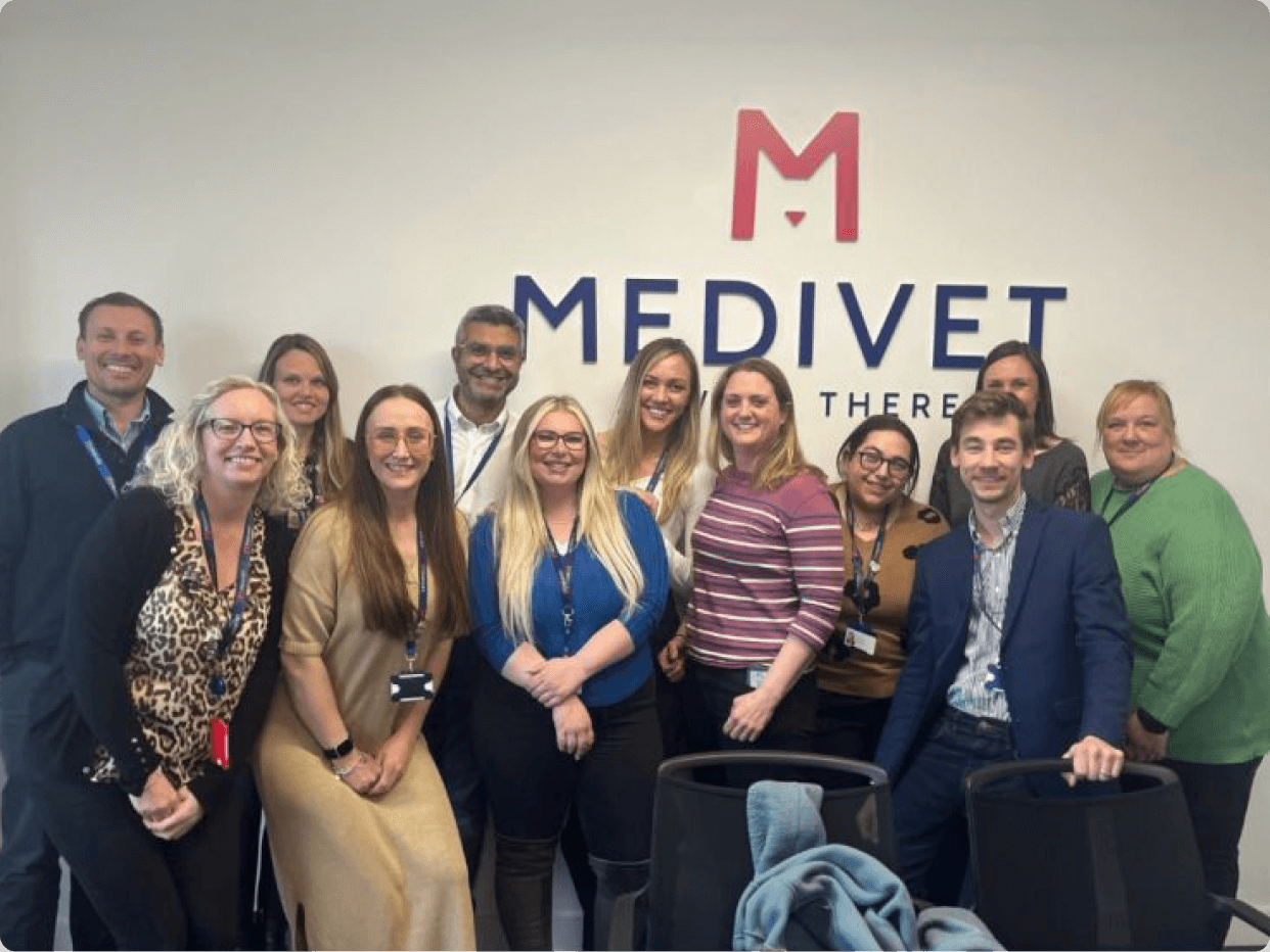 A group of twelve diverse professionals poses together in front of a MEDIVET sign, showcasing collaboration and teamwork in a modern workspace.
