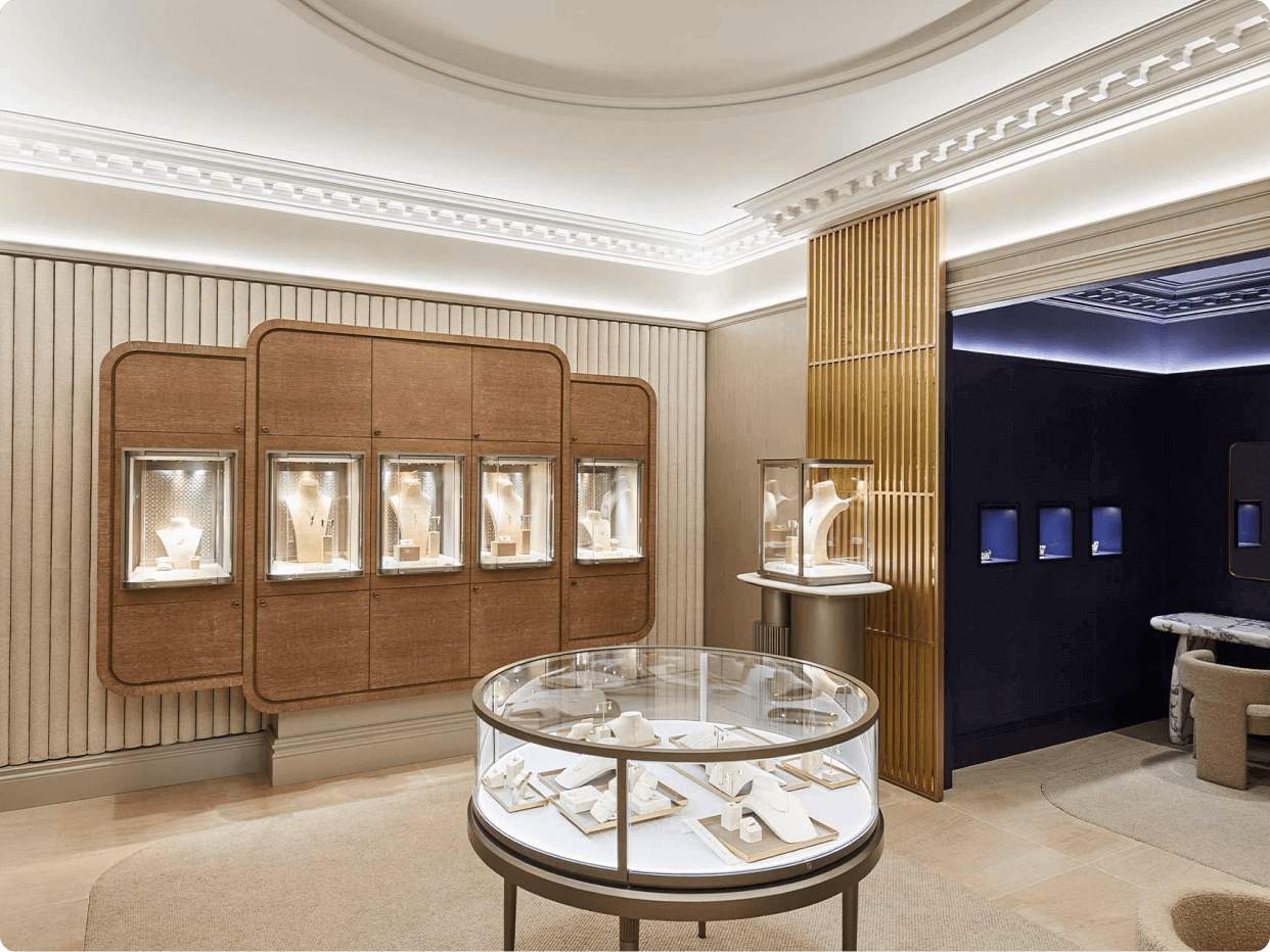 A sophisticated jewelry showroom featuring glass display cases against wooden paneling and a central glass table showcasing various pieces, illuminated by soft lighting for an elegant ambiance.