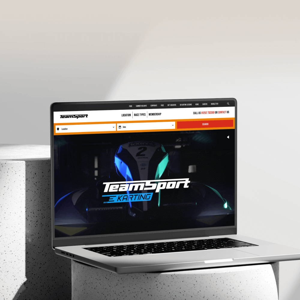 A laptop displaying the TeamSport Karting website, featuring racing graphics and vibrant colors, sits on a modern, minimalist surface.