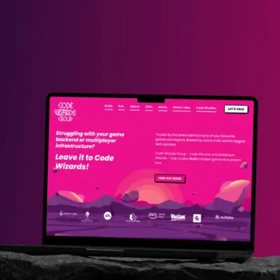 Laptop displaying the vibrant magenta homepage of Code Wizards Group, promoting game backend and multiplayer infrastructure services. The screen shows text about the company and icons of partner logos at the bottom, set against a gradient background.