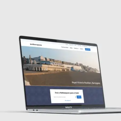 A laptop displaying a website with a large image of a seaside building labeled "Royal Victoria Pavilion, Ramsgate." The page includes menus and a search bar for finding pubs. The laptop rests on a plain background.