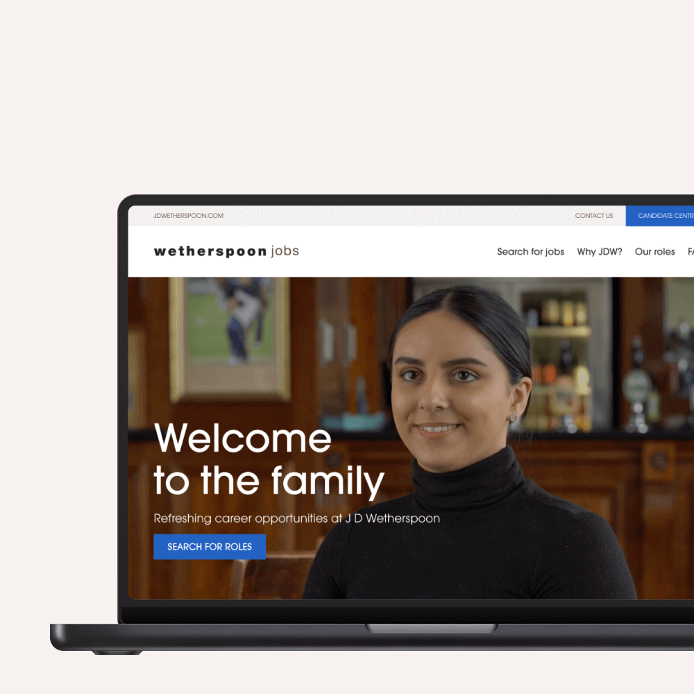 A laptop displays the Wetherspoon jobs website featuring a welcoming message and a smiling female employee, inviting users to explore career opportunities at JD Wetherspoon.