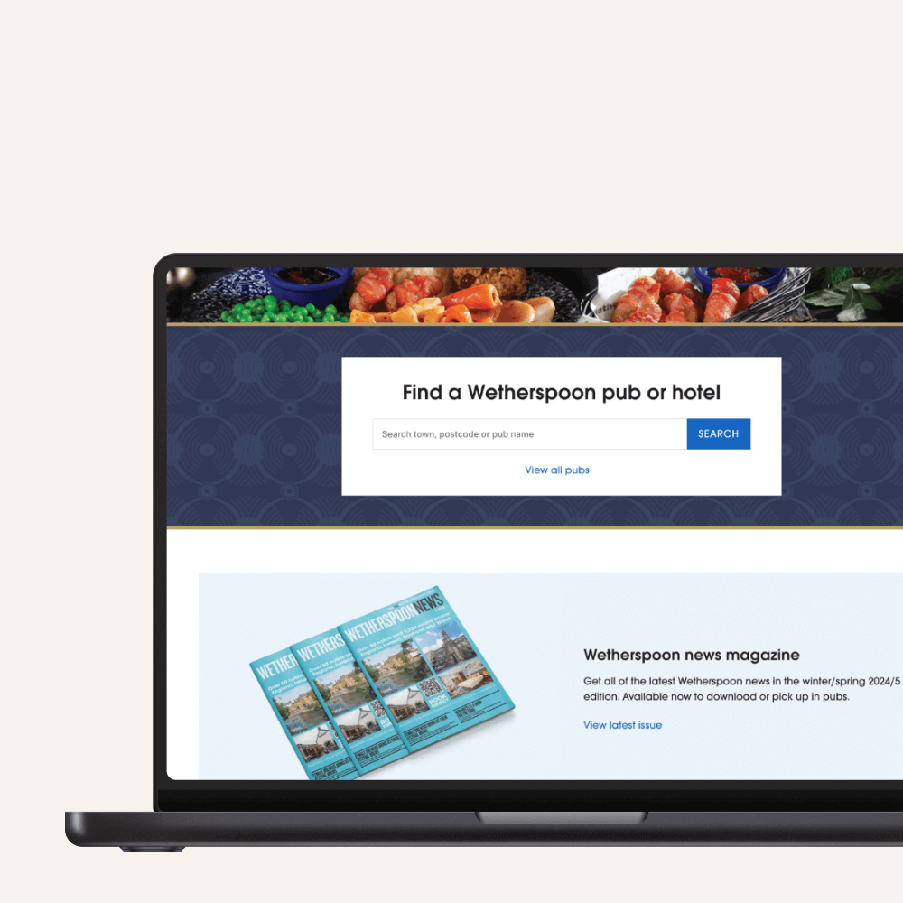 A laptop screen displays a website where users can search for Wetherspoon pubs or hotels. The page features images of food, a search bar, and a link to the Wetherspoon news magazine.