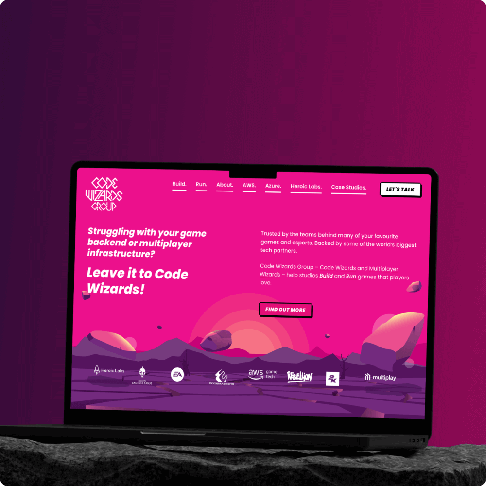 A laptop displays a vibrant pink website for Code Wizards, promoting services for game backend and multiplayer infrastructure support. The design features playful graphics and bold text inviting users to explore their solutions.