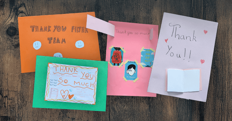 Four colorful handmade thank-you cards with various decorations and messages on a wooden surface.