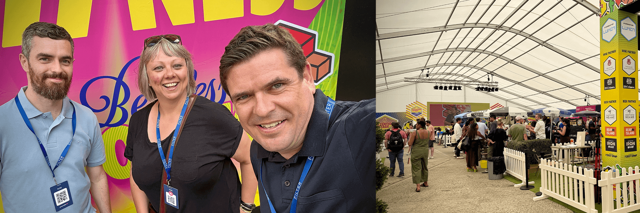 Three people with blue lanyards smile in front of a colorful banner, with a large indoor event space in the background featuring booths and attendees.
