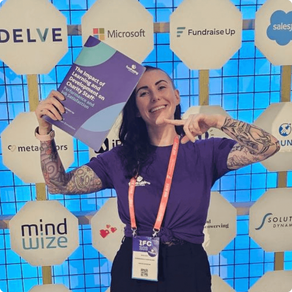 A person with tattoos holds a report while smiling and posing in front of a backdrop featuring various company logos.