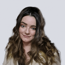A person with long, wavy hair is smiling slightly, facing the camera against a plain background.