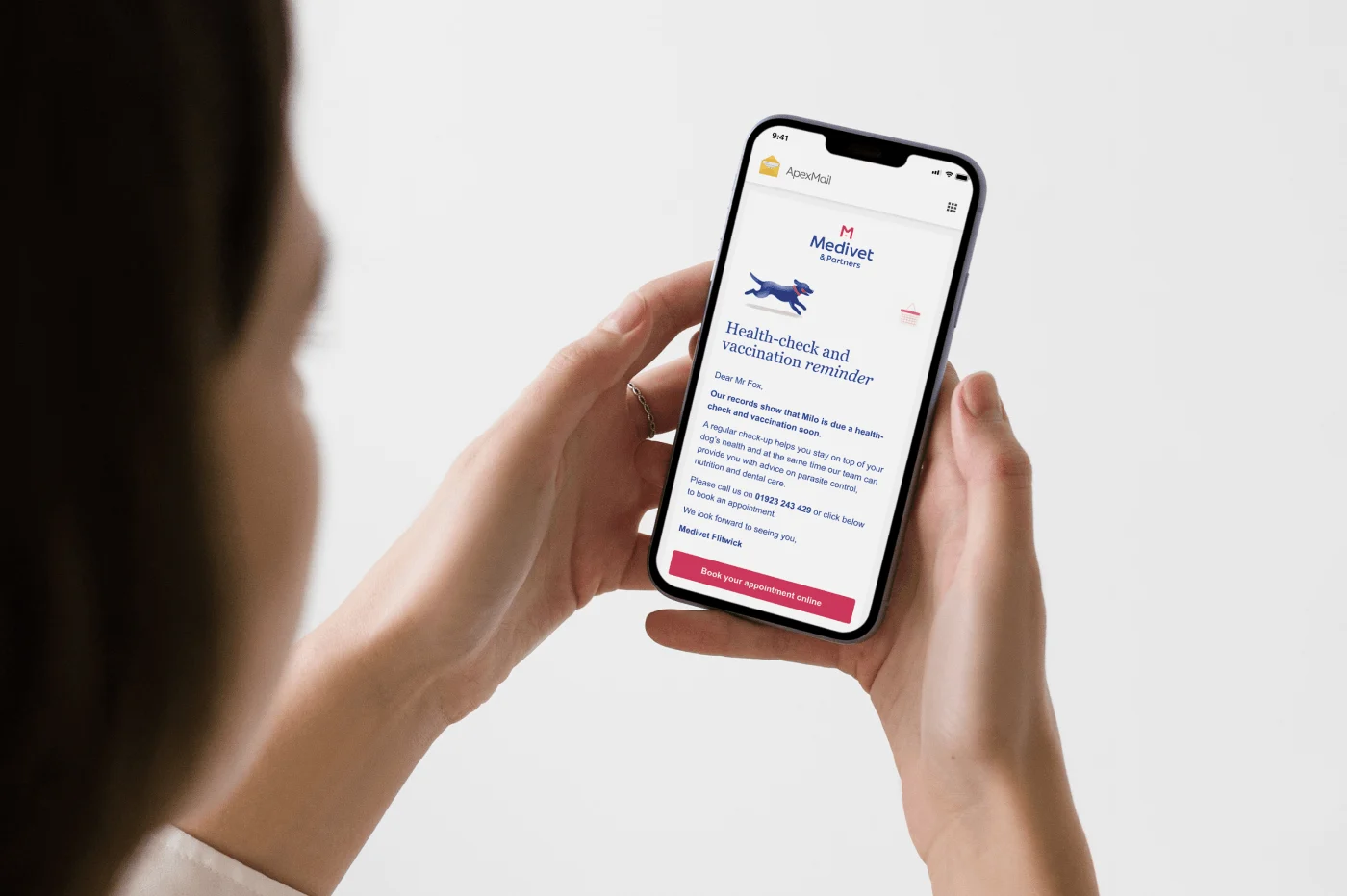 A woman holds a smartphone showing a Medivet email in the ApexMail app – a health-check and vaccination reminder for a dog named Milo, with a running dog illustration and a "Book your appointment online" button.